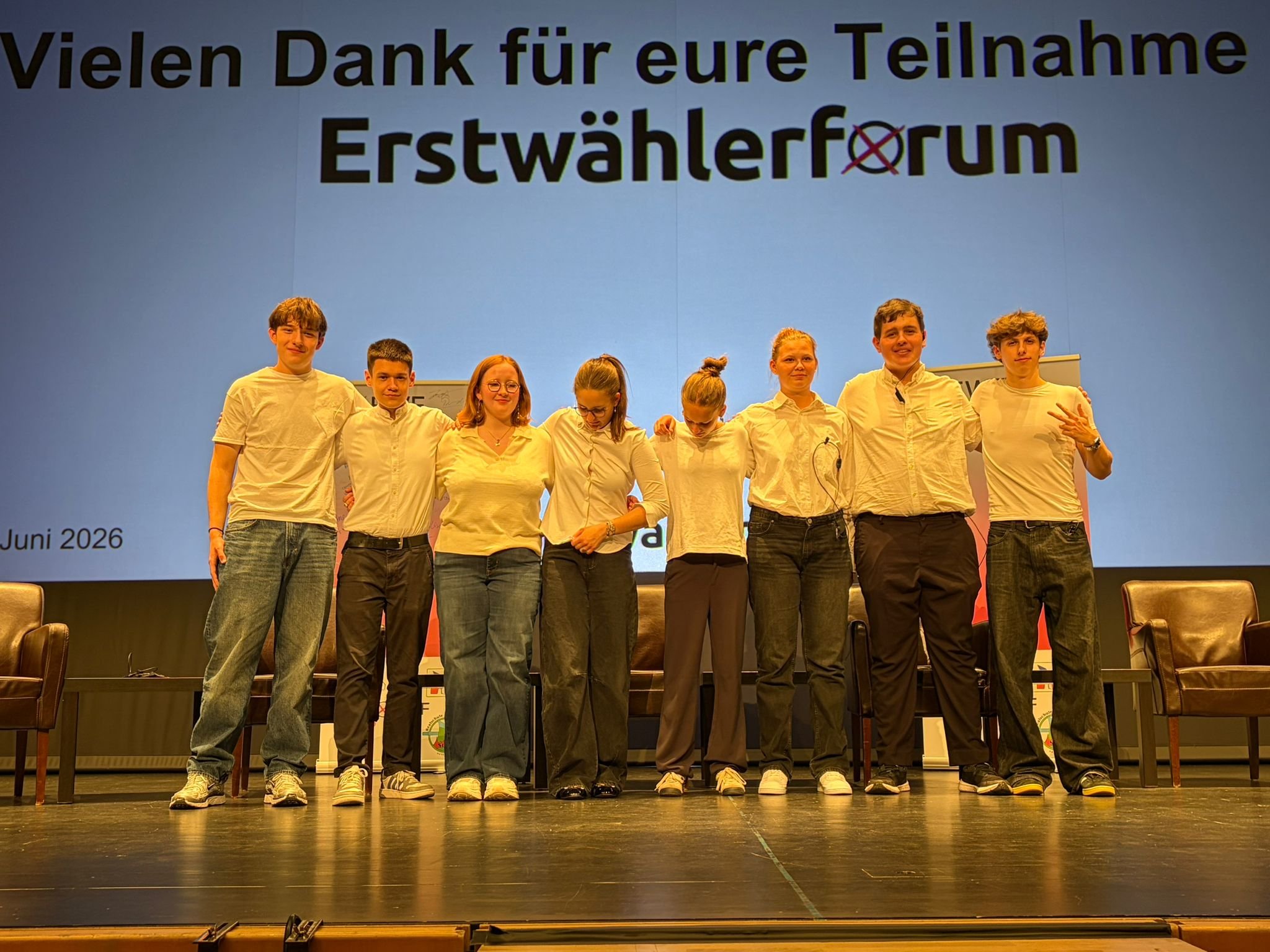 Das Leitungsteam des EWF26 steht auf einer Bühne vor einer Projektion mit dem Schriftzug „Erstwählerforum“.