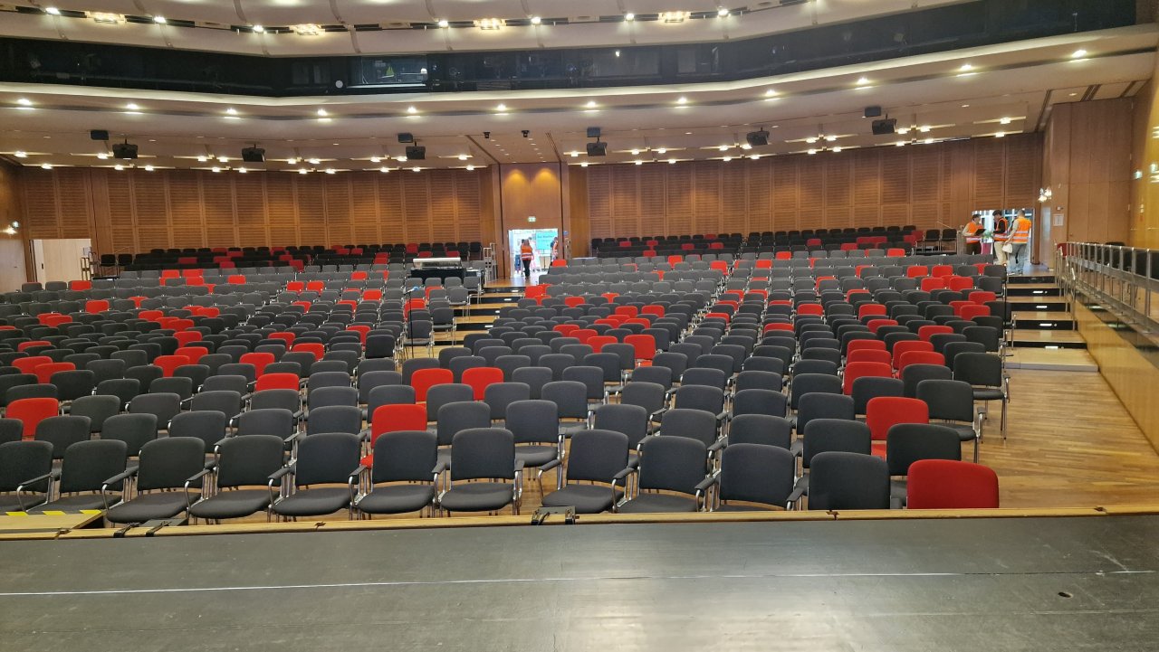 Reihen grauer und roter Sitze im noch leeren Veranstaltungssaal.