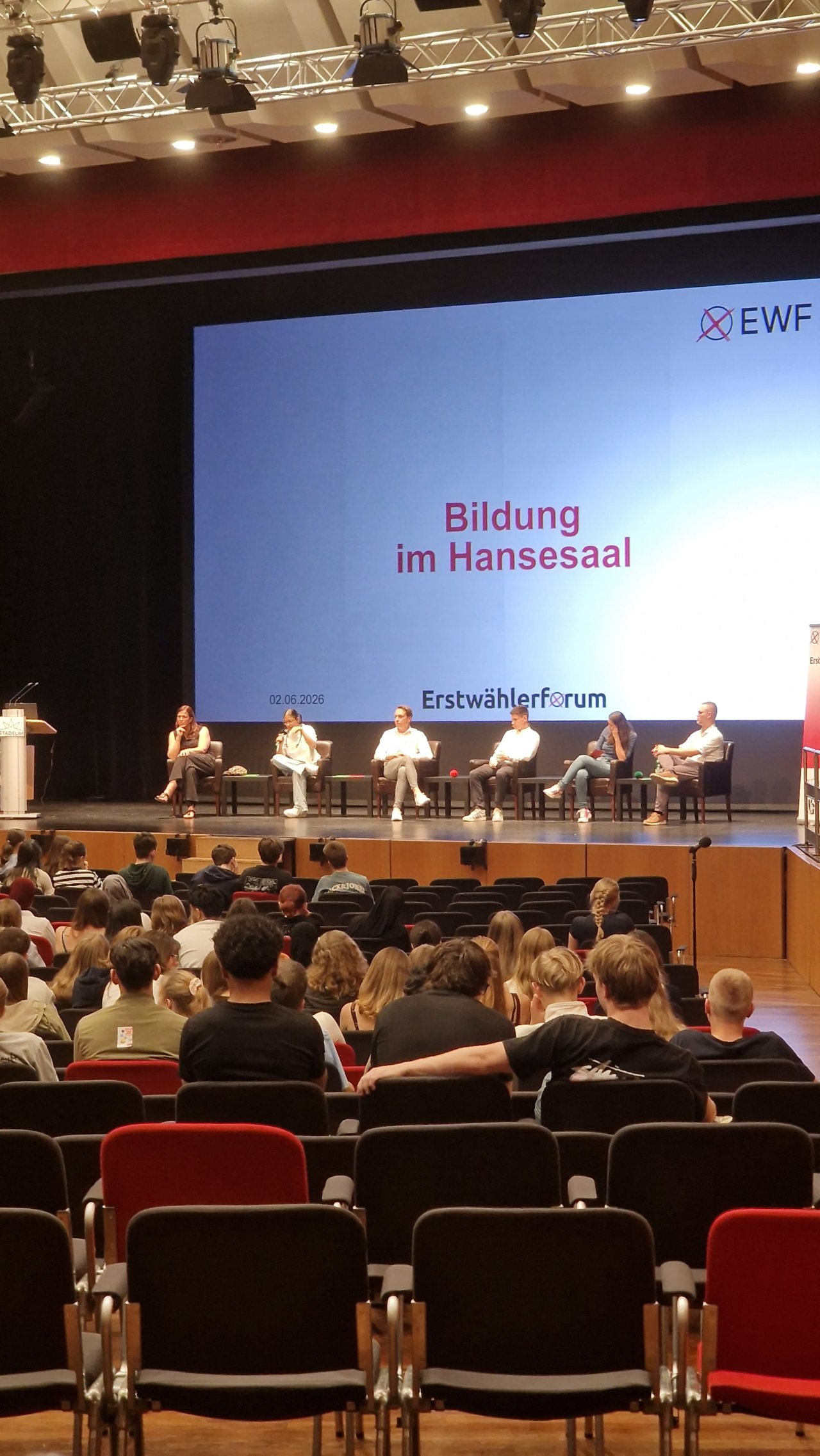 Bildungspodium auf der Bühne, zwischen den Sitzreihen fotografiert.