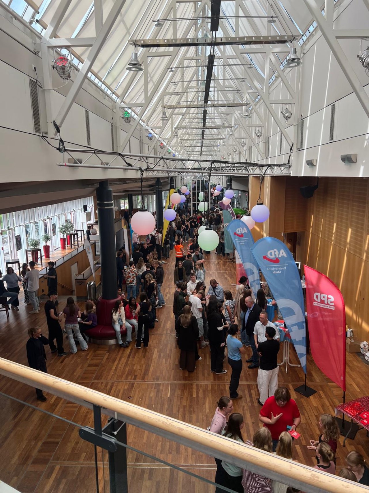 Besucherinnen und Besucher zwischen Parteiständen im Foyer unter dem Glasdach.