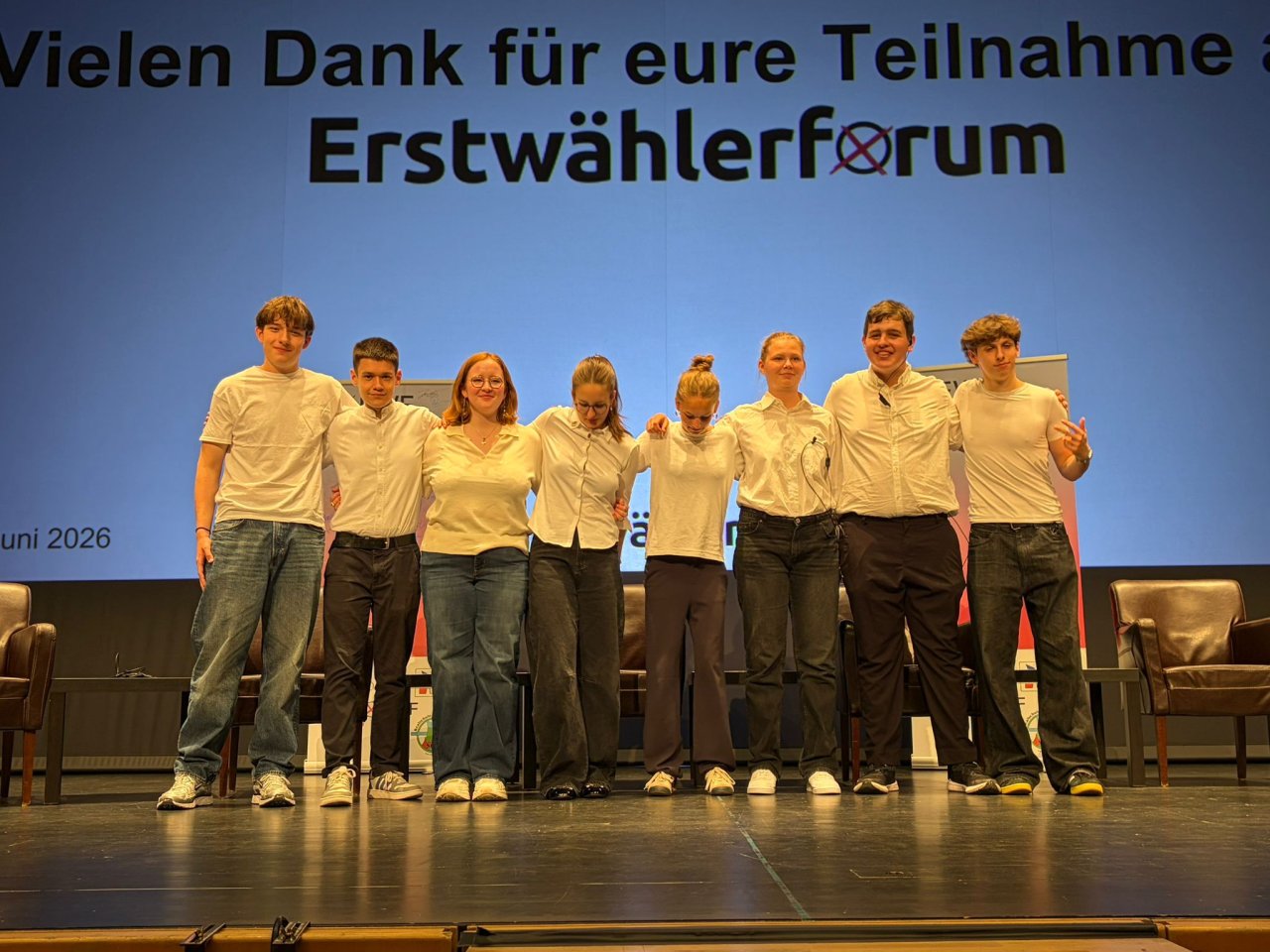 Gruppe in weißen Hemden nebeneinander auf der Bühne.