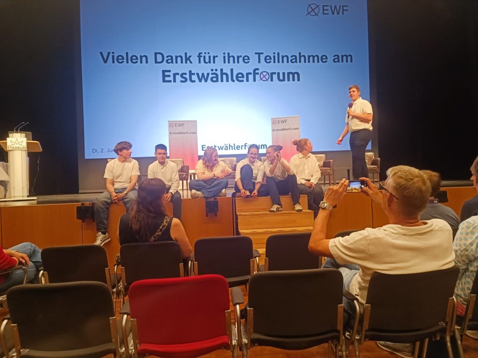 Abschluss des Erstwählerforums mit einer Gruppe auf der Bühne und einem Redner mit Mikrofon.