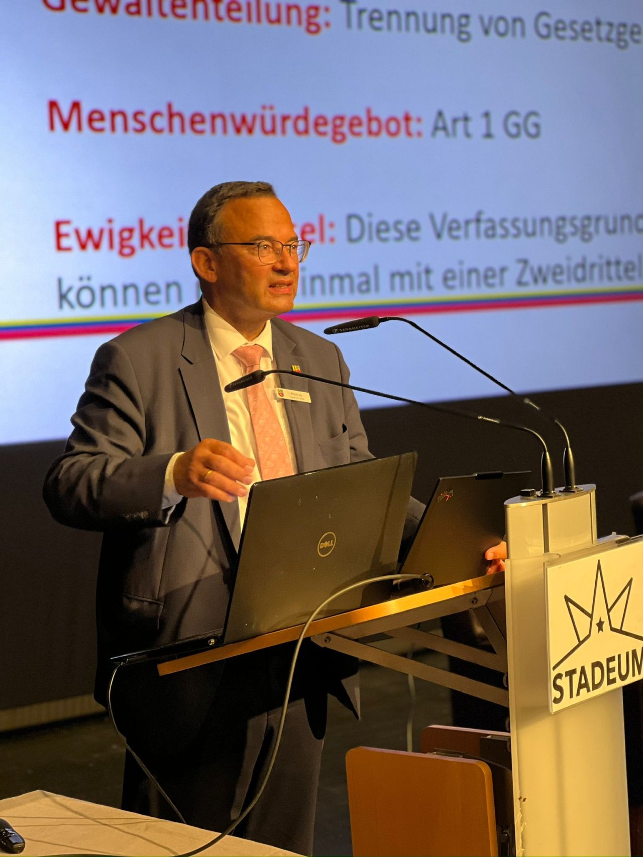 Redner am Pult vor einer Präsentation über das Grundgesetz.