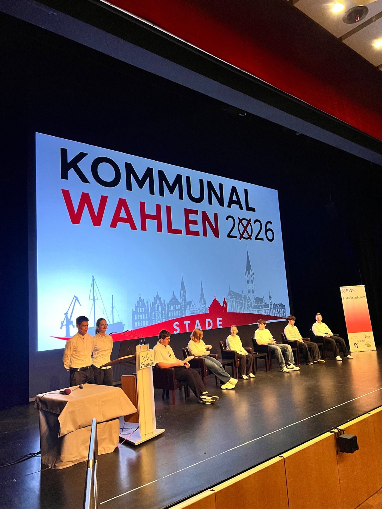 Podium auf der Bühne vor einer Präsentation zu den Kommunalwahlen 2026.